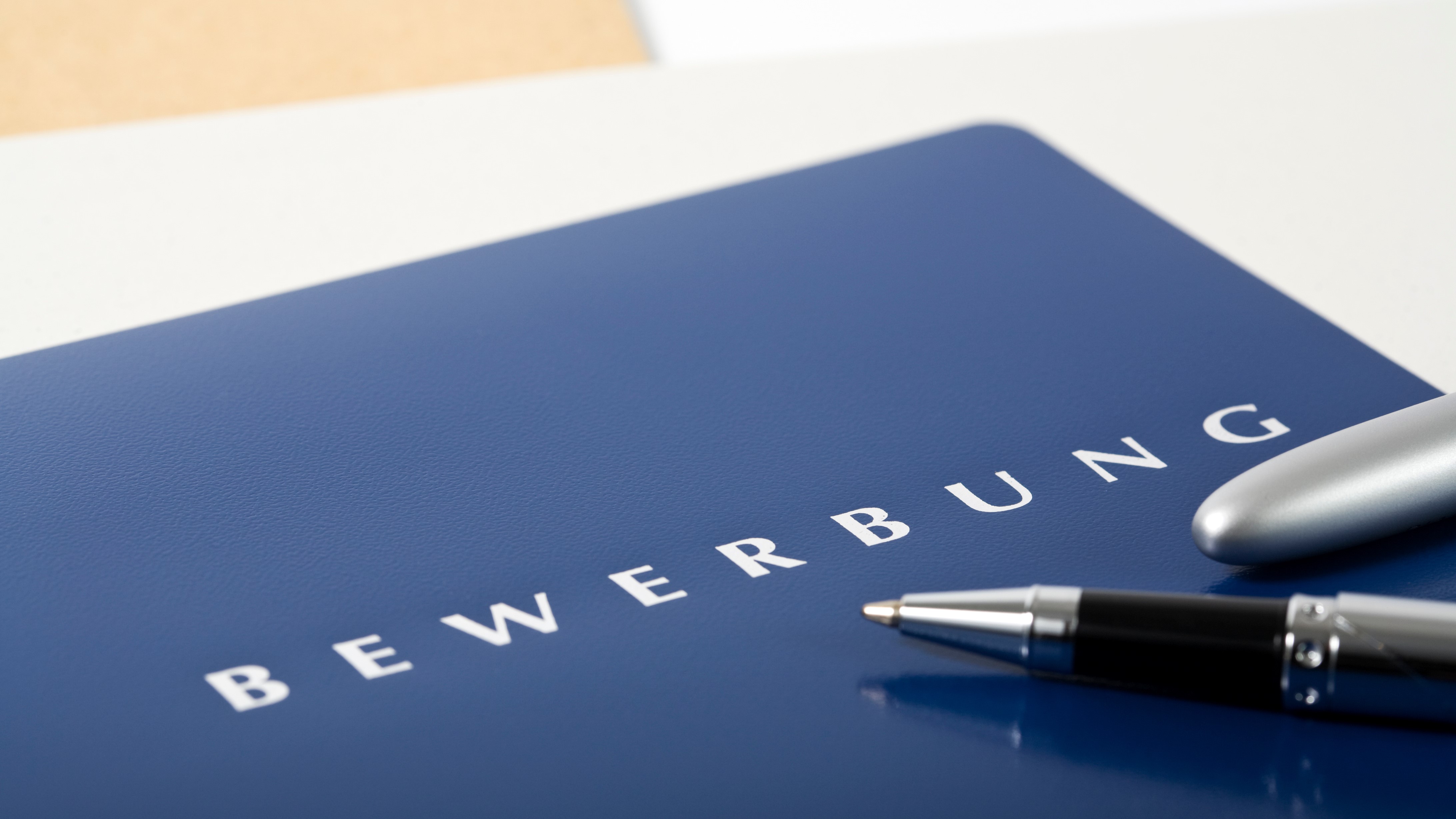 Bewerbungsmappe mit Stift neben Laptop