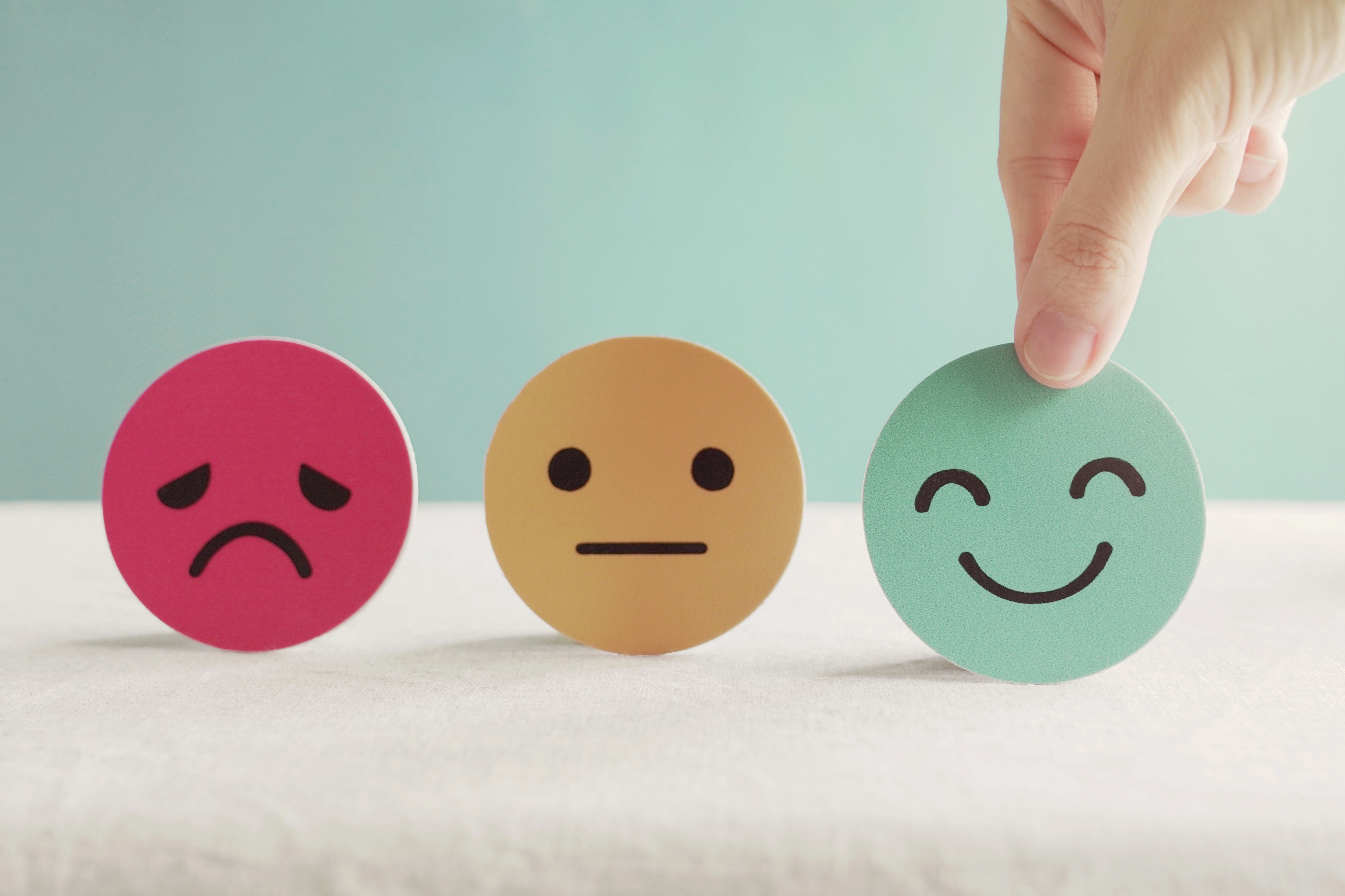 Drei Smileys, traurig, neutral und lachend. Hand greift nach lachendem Smiley.
