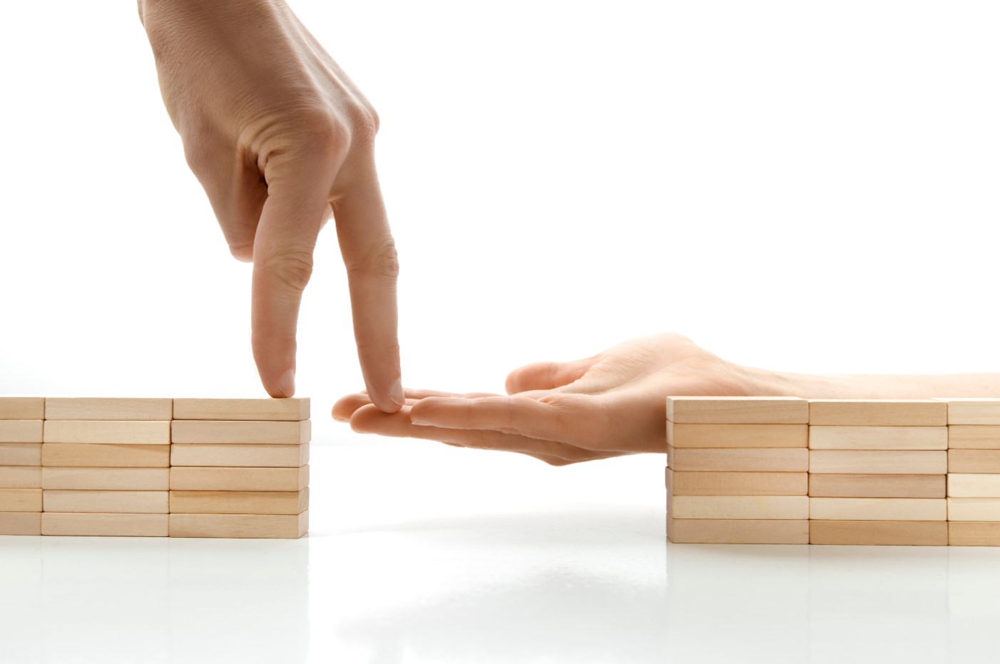 Zwei Hände überbrücken mit Fingern eine Lücke zwischen zwei kleinen Holztürmen.
